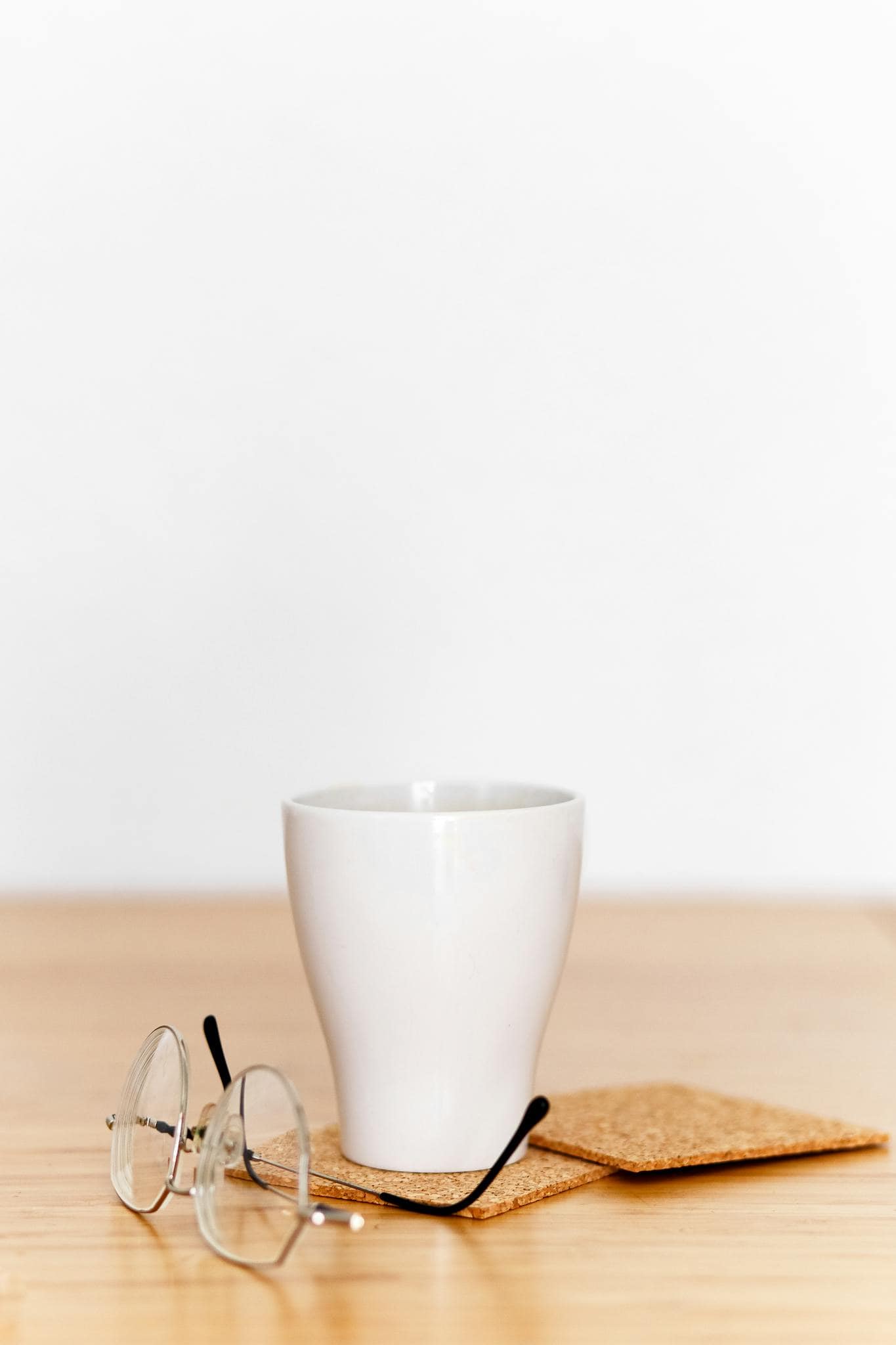 A minimalist setup of a white coffee cup and eyeglasses on a wooden table, perfect for lifestyle themes.