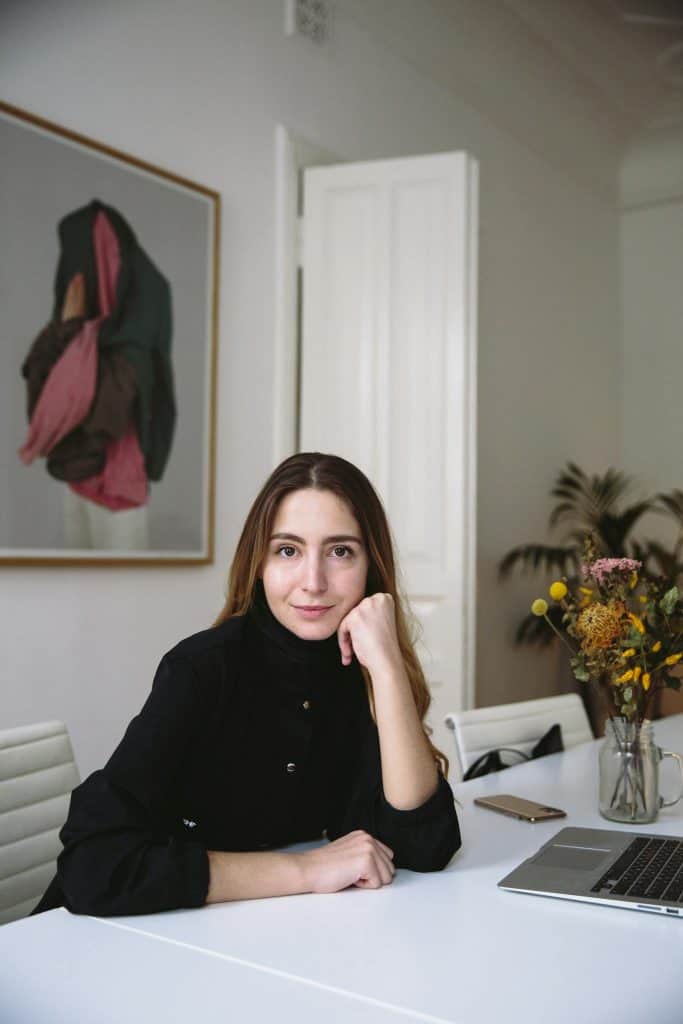 Portrait of a woman in a modern office setting, seated at a desk with a laptop.