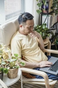Mature man engaged in remote work, surrounded by lush indoor plants by a sunny window.