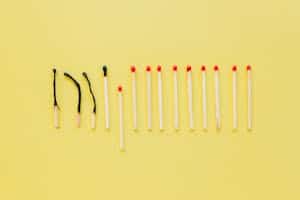 Artistic flat lay of burnt and unlit matches on a yellow surface, symbolizing burnout.