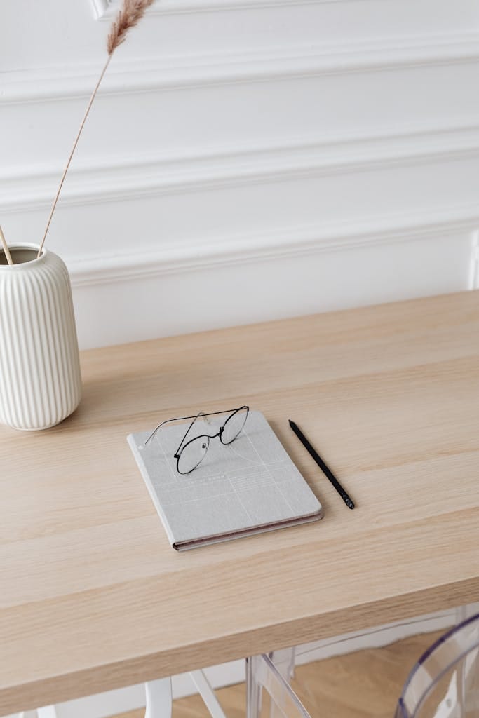 Minimalist desk with a notebook, eyeglasses, and a pen on a wooden table for a simple workspace.