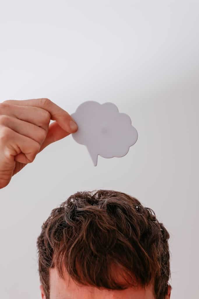 Person holds blank speech bubble above head, white background.