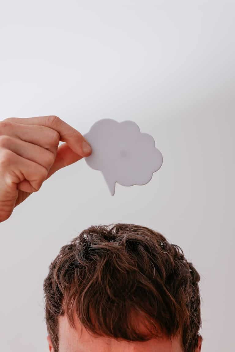 Person holds blank speech bubble above head, white background.
