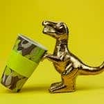 Souvenir in form of gilded shiny dinosaur with tilted cup composed on yellow background