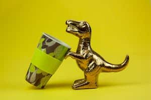 Souvenir in form of gilded shiny dinosaur with tilted cup composed on yellow background