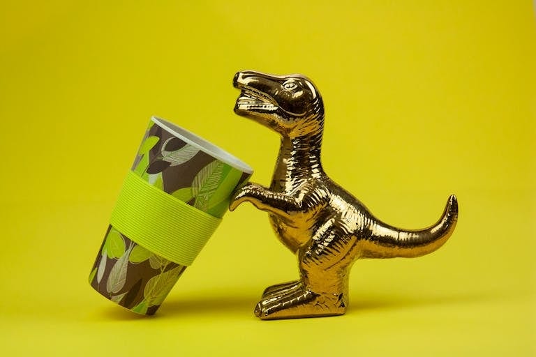Souvenir in form of gilded shiny dinosaur with tilted cup composed on yellow background